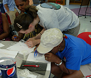 Researchers and community members at a table examine specimens, using tweezers and magnifying glasses.